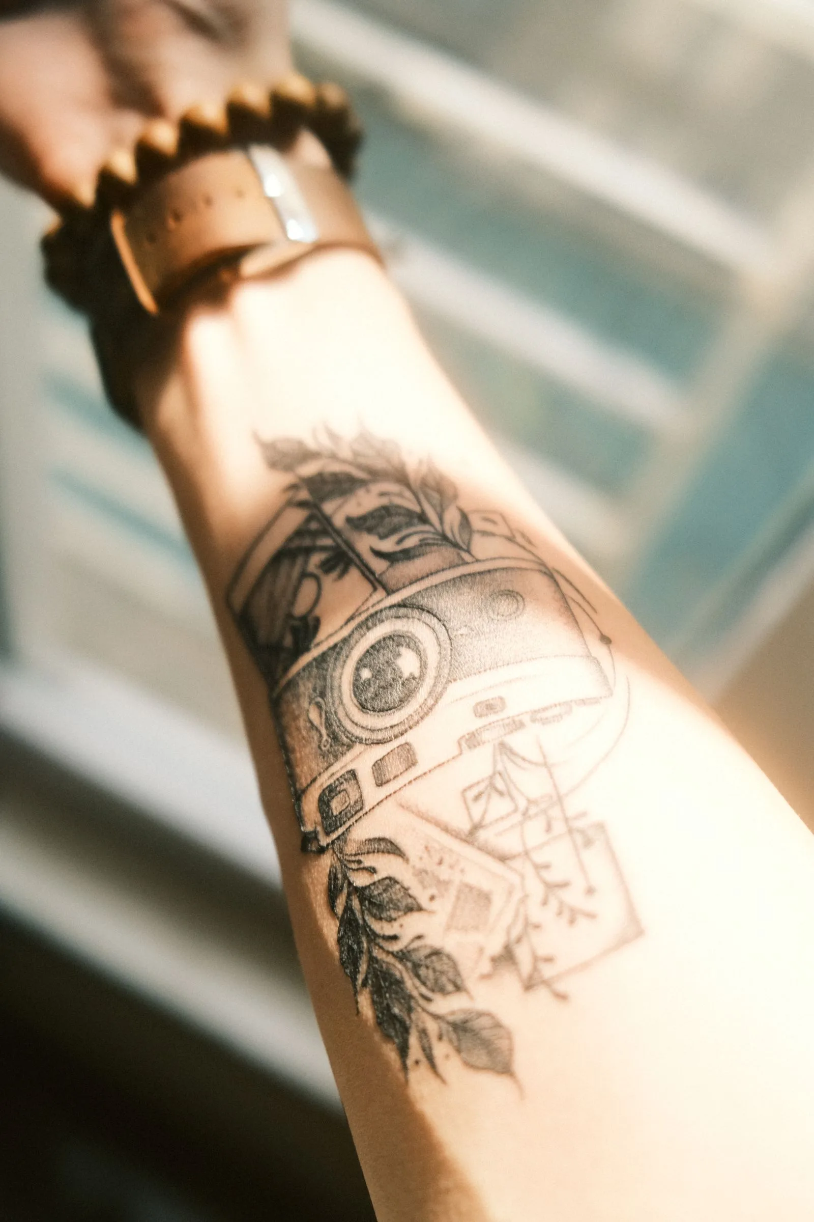 Onderarm met een tattoo van een fototoestel en bladeren