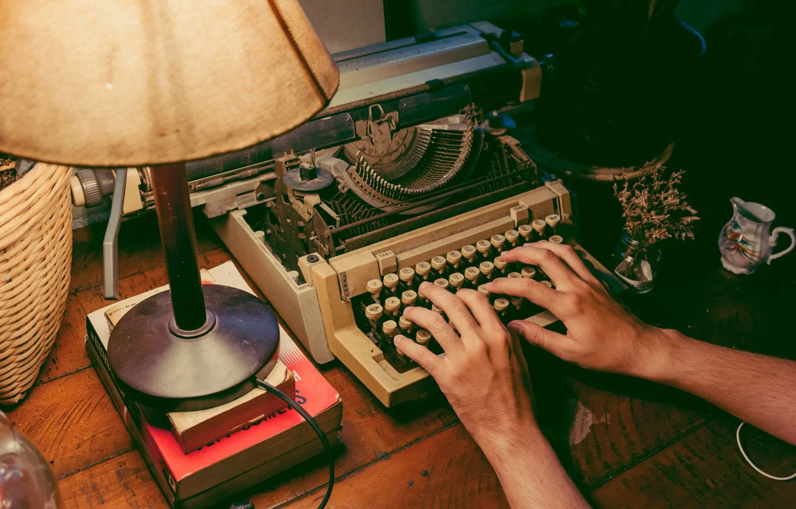 Handen op een oude typemachine naast een leeslamp