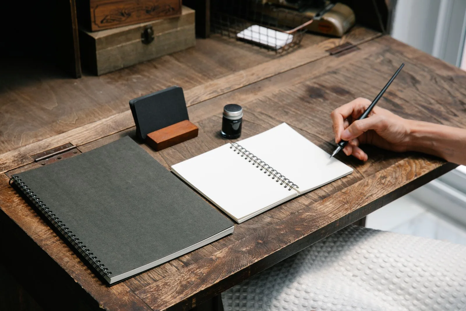 Iemand schrijft in een notitieboek aan een houten bureau