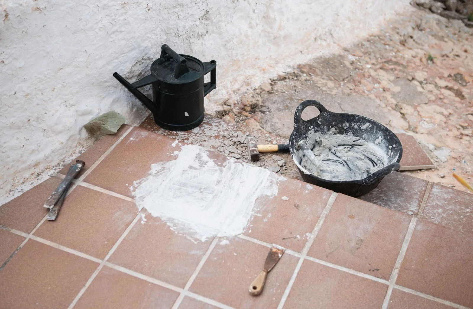 Troffel, voegspaan en mortel op een terracotta tegelvloer