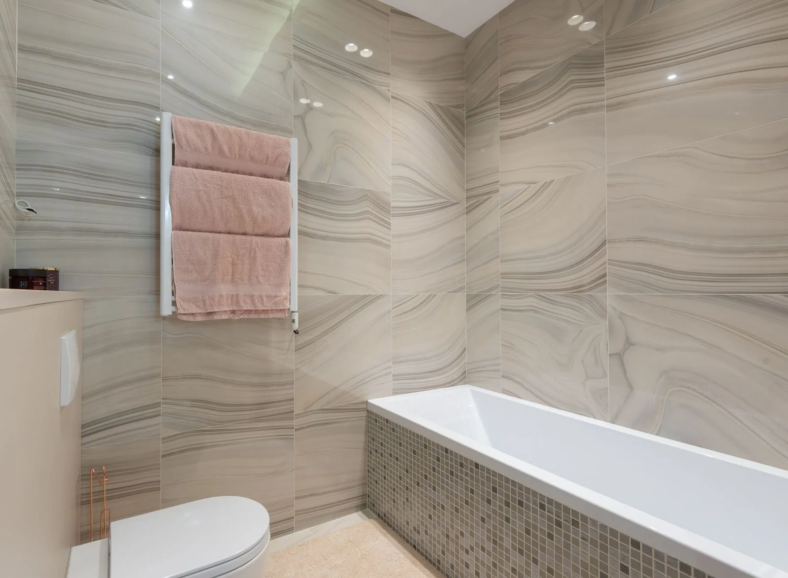 Badkamer met grote wandtegels en een mozaïek rond het bad