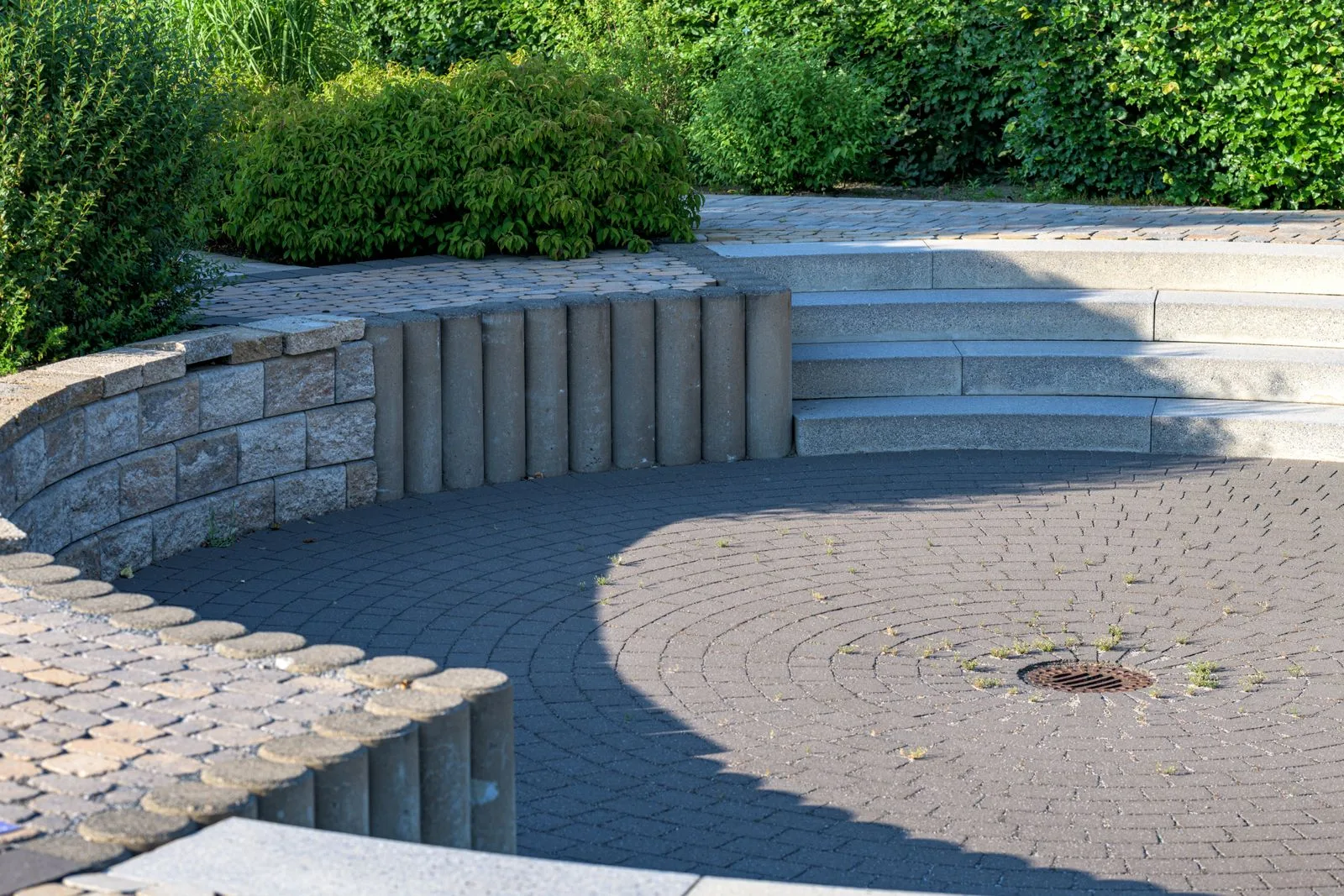 Een rond terras in kasseien met een zitmuur in natuursteen